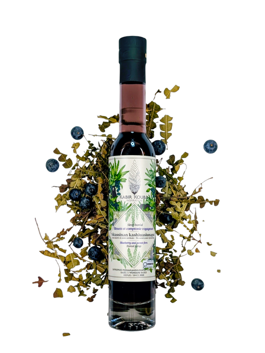 Bouteille de sirop boréal bleuet et comptonie voyageuse 200 ml par Kabir Kouba Inspiration, entourée de bleuets et de feuilles de comptonie